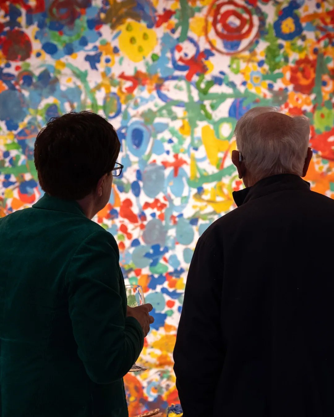 Two visitors seen from behind looking at a large, colourful painting